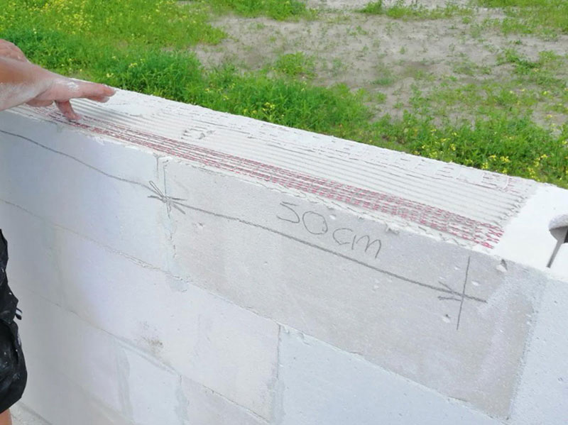 Zbliżenie na ścianę z betonu komórkowego z wykonanym zbrojeniem podokiennym i zaznaczeniem wymiaru 50 cm.
